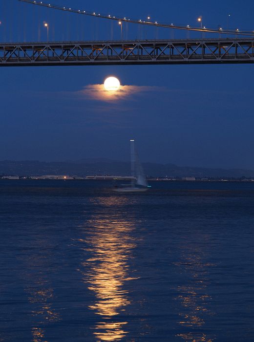 The moon reflects on the water as a boat sails by